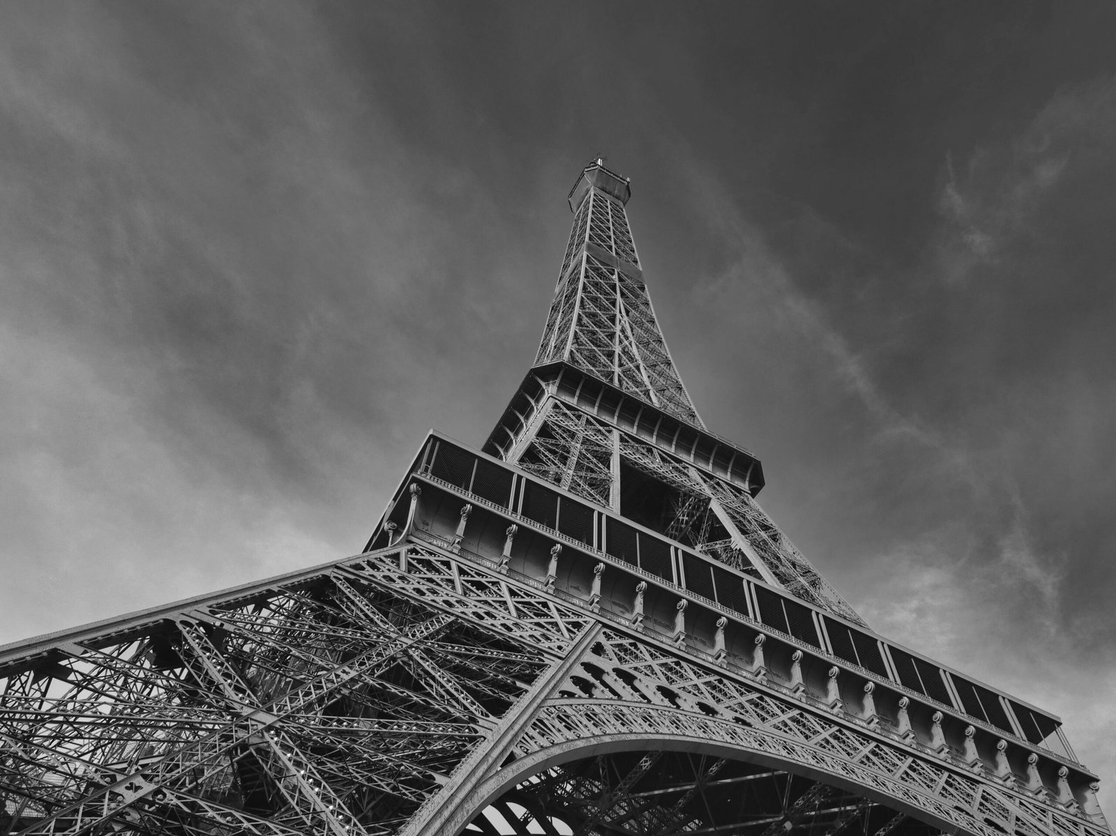 Dramatic low angle view of the Eiffel Tower in Paris, showcasing intricate steel design against a cloudy sky.